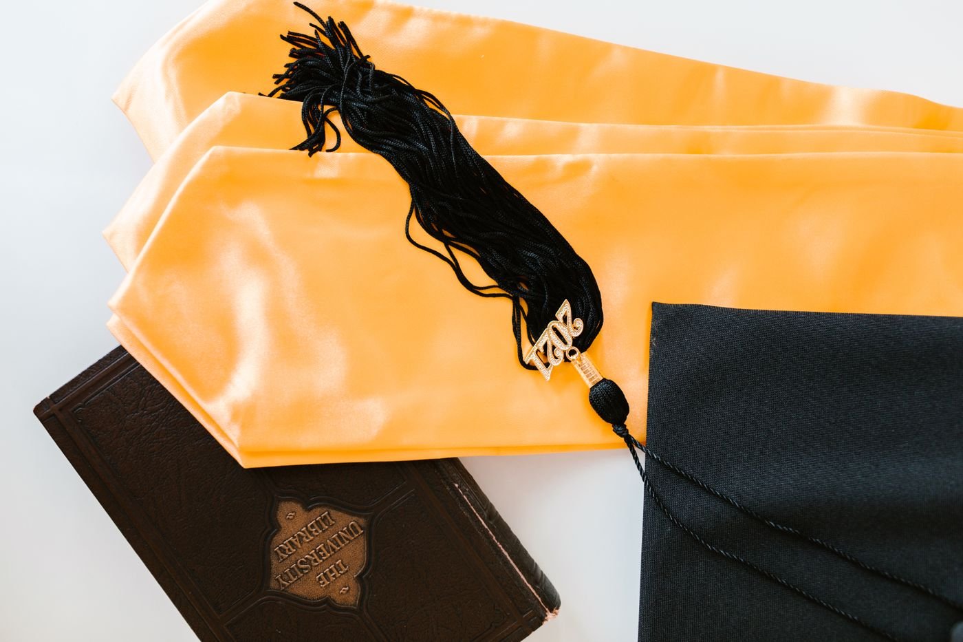 A graduation cap, tassel and an old library book on a white table