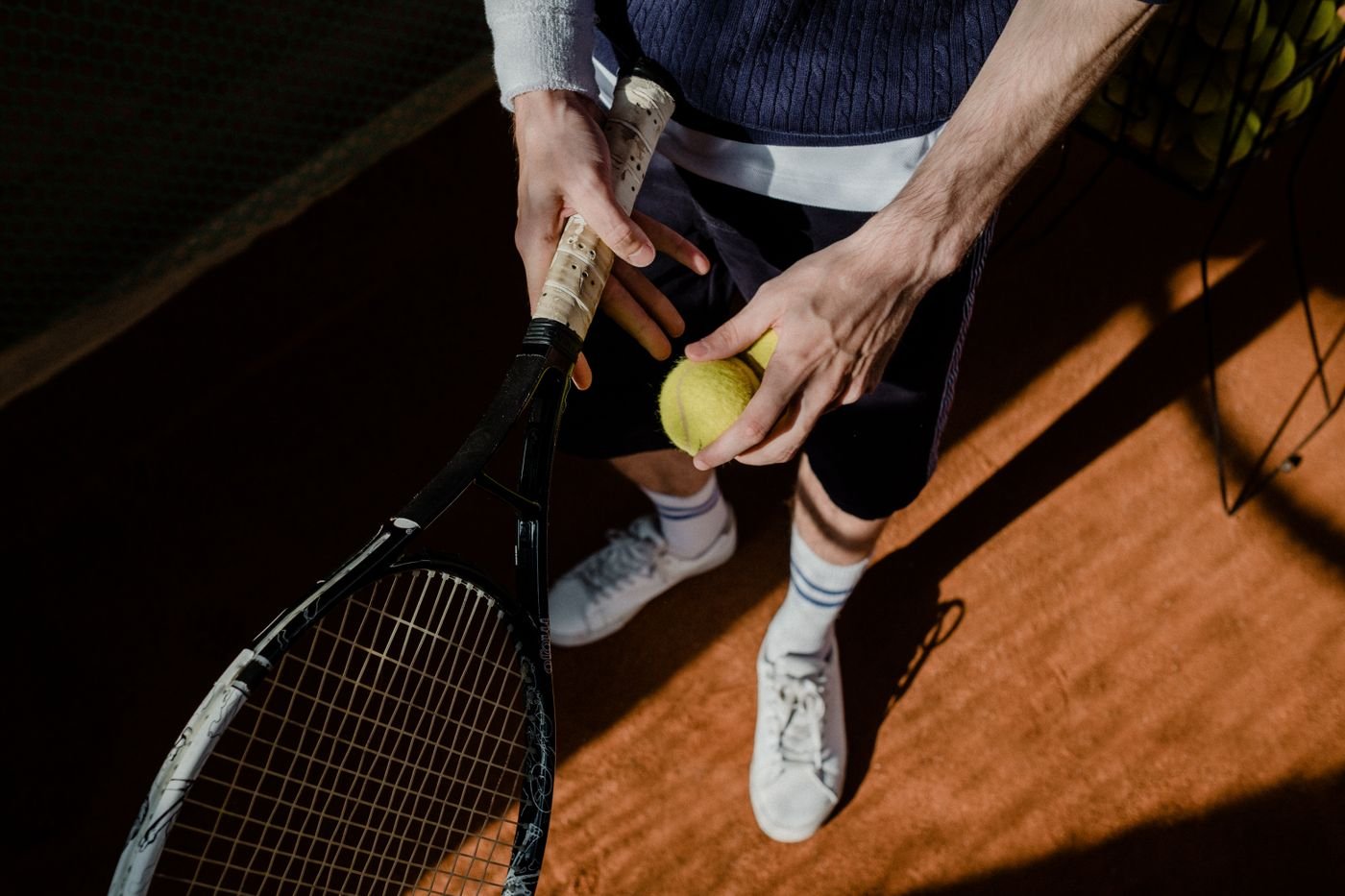 Close-up of a tennis player's hands holding a racket and ball on a clay court